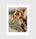 Flip by Muse and Paw, a painterly print of a cocker spaniel held upside down by its owner, framed and leaning against a wall.