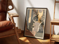 Front Page by Muse and Paw, a print of a black French bulldog reading a newspaper on a pink toilet, framed and leaning against a sunlit wall beside a leather chair and wooden shelving.