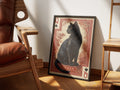 Her Majesty by Muse and Paw, a print of a black cat as the Queen of Spades on a red card, framed and styled in a sunlit room with a leather armchair and wooden shelving.