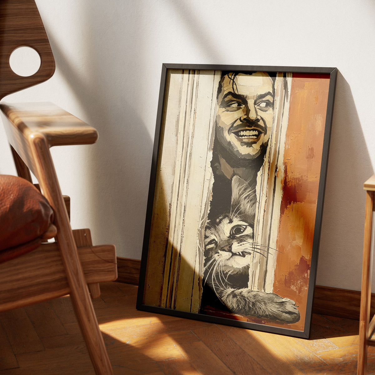 Let Me In by Muse and Paw, a painterly print of a grinning face and a grey tabby cat both pressed into the gap of a splintered door, framed and leaning against a wall in sunlight.
