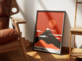Mount Neko by Muse and Paw, a minimalist red and black poster of a mountain shaped like a cat, framed and styled in a sunlit room with a leather armchair and wooden shelving.