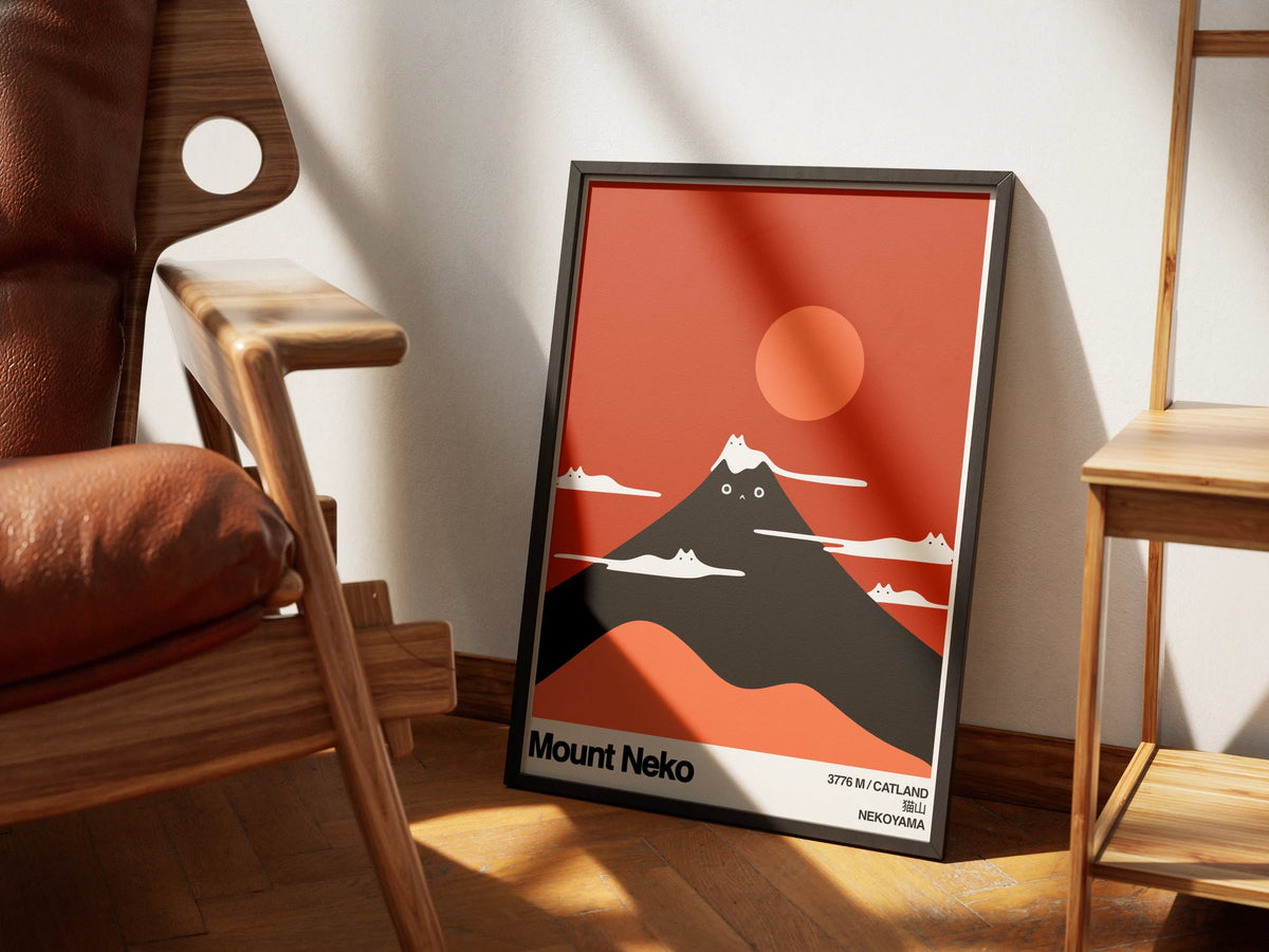 Mount Neko by Muse and Paw, a minimalist red and black poster of a mountain shaped like a cat, framed and styled in a sunlit room with a leather armchair and wooden shelving.
