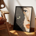 One Soul by Muse and Paw, a print splitting the frame between a black cat's face and a woman's face joined seamlessly at the nose, framed and leaning against a wall.