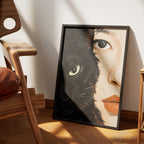 One Soul by Muse and Paw, a print splitting the frame between a black cat's face and a woman's face joined seamlessly at the nose, framed and leaning against a wall.