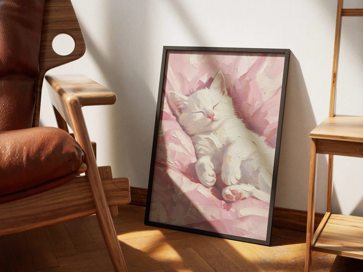 Petal by Muse and Paw, a palette knife print of a white kitten asleep on a pink blanket, framed and styled in a sunlit room with a leather armchair and wooden shelving.