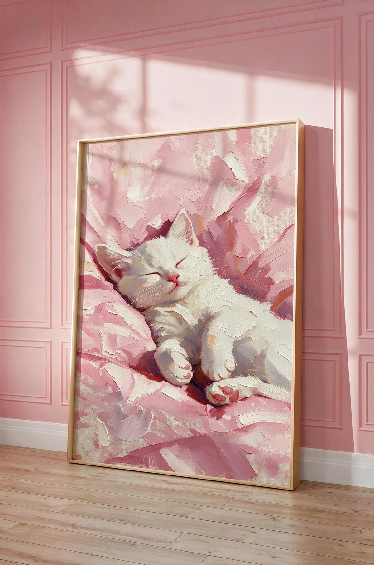 Petal sleeping white kitten wall art in a gold frame, leaning against a pink panelled wall on a wooden floor.