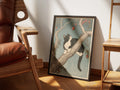 Pomegranate by Muse and Paw, a print of a tuxedo cat resting in a pomegranate tree against a blue sky, framed and leaning against a sunlit wall beside a leather chair and wooden shelving.