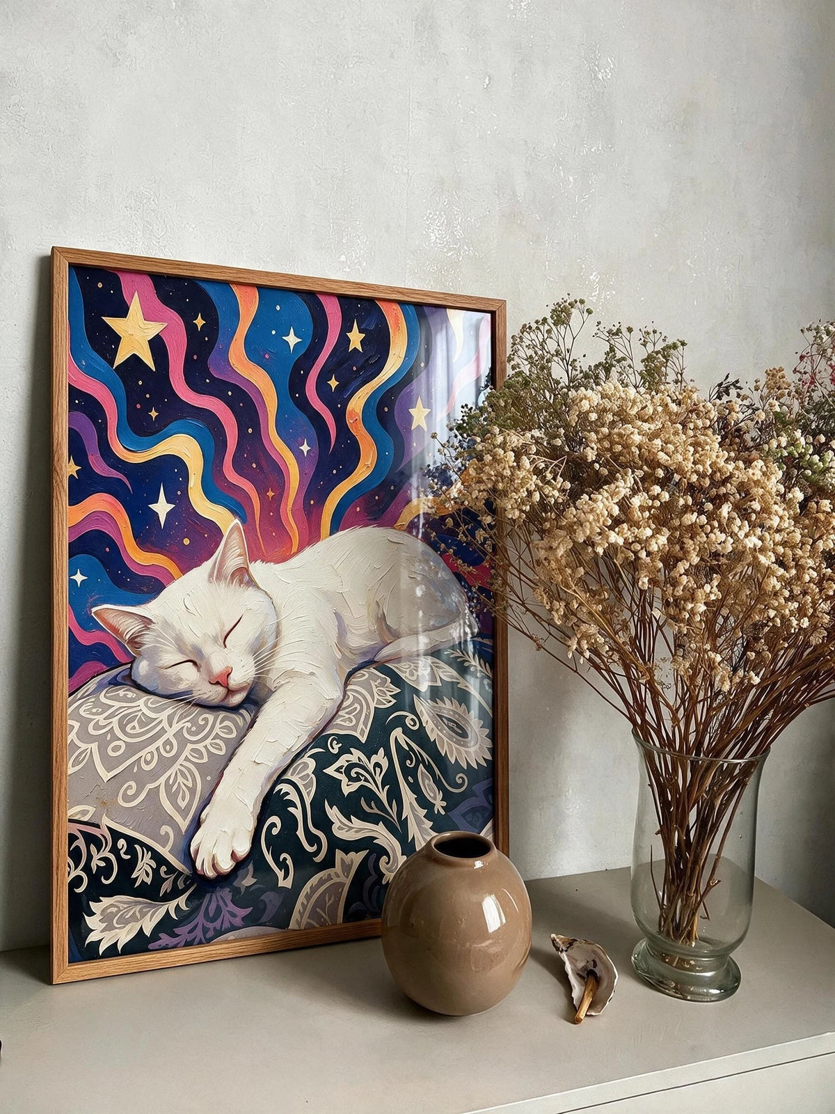 Reverie white cat starry night wall art in an oak frame, resting on a console beside a vase of dried flowers.