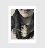 Stowaway by Muse and Paw, a close-up print of a kitten peeking out from a wool scarf, framed and leaning against a wall.