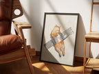 Stuck by Muse and Paw, a painterly print of a ginger cat taped to a pale wall, framed and styled in a sunlit room with a leather armchair and wooden shelving.