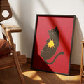 Sunspot by Muse and Paw, a print of a black cat lying on its back on a deep red ground, holding a small golden sun against its chest, framed and leaning against a wall.